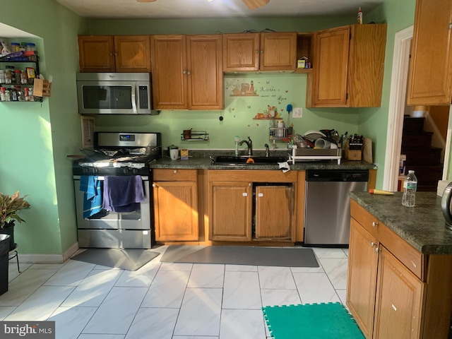 kitchen featuring baseboards, appliances with stainless steel finishes, brown cabinetry, and a sink