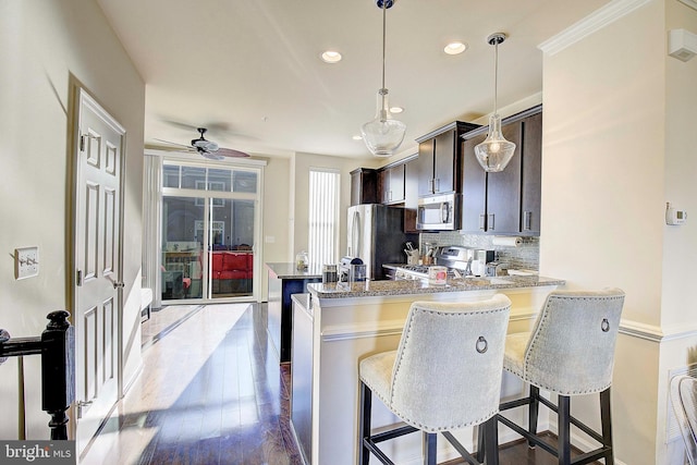 kitchen featuring dark wood-style flooring, decorative backsplash, appliances with stainless steel finishes, a peninsula, and a kitchen breakfast bar