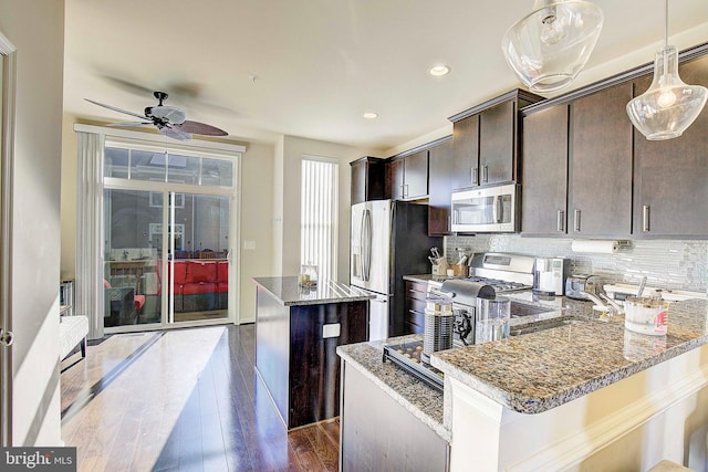 kitchen with dark wood finished floors, stainless steel appliances, tasteful backsplash, a kitchen island, and dark brown cabinetry