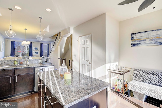 kitchen with dishwasher, ceiling fan, light stone counters, dark brown cabinets, and a sink