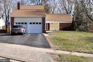 view of front of property with asphalt driveway, a garage, a chimney, and a front yard