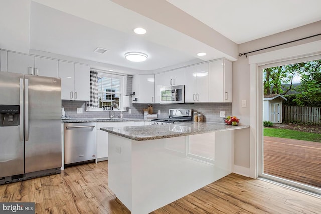 kitchen with appliances with stainless steel finishes, a sink, a peninsula, light wood-style flooring, and recessed lighting