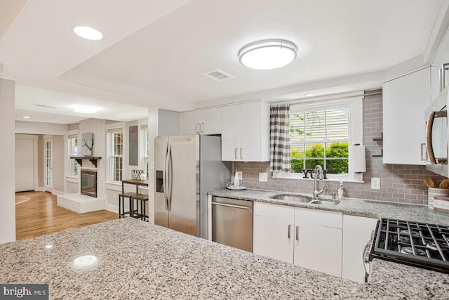 kitchen featuring stainless steel appliances, a sink, backsplash, light stone counters, and recessed lighting