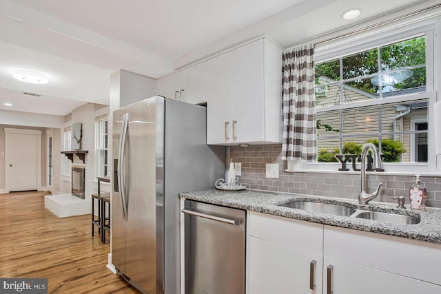 kitchen with appliances with stainless steel finishes, a sink, white cabinetry, backsplash, and light wood-style flooring