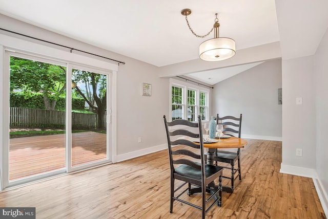 dining space featuring baseboards, light wood-style flooring, and vaulted ceiling
