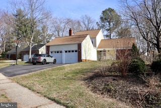 view of side of home featuring asphalt driveway, a chimney, and a garage