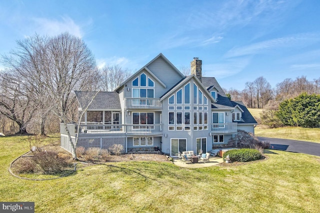 rear view of property with a deck, a patio, a lawn, and a chimney