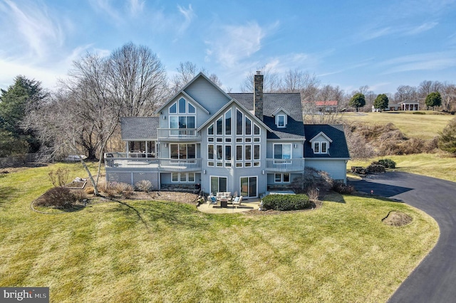 rear view of property with a lawn, a chimney, a balcony, driveway, and a patio