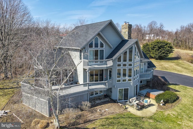 rear view of property with a shingled roof, a balcony, a lawn, and a chimney