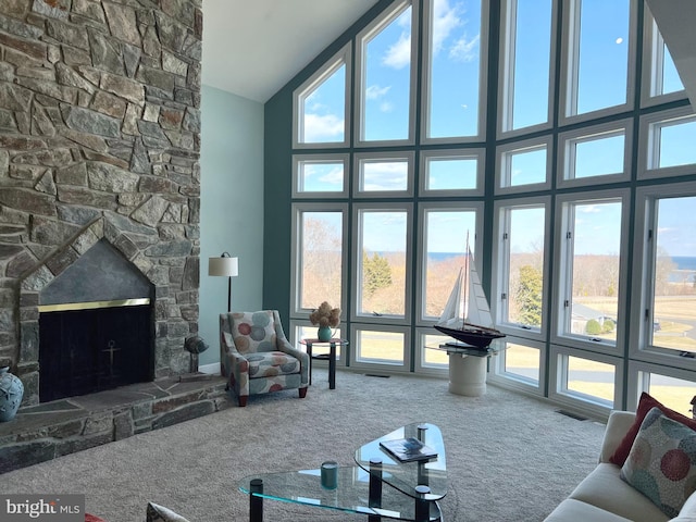 carpeted living area with visible vents, plenty of natural light, high vaulted ceiling, and a stone fireplace