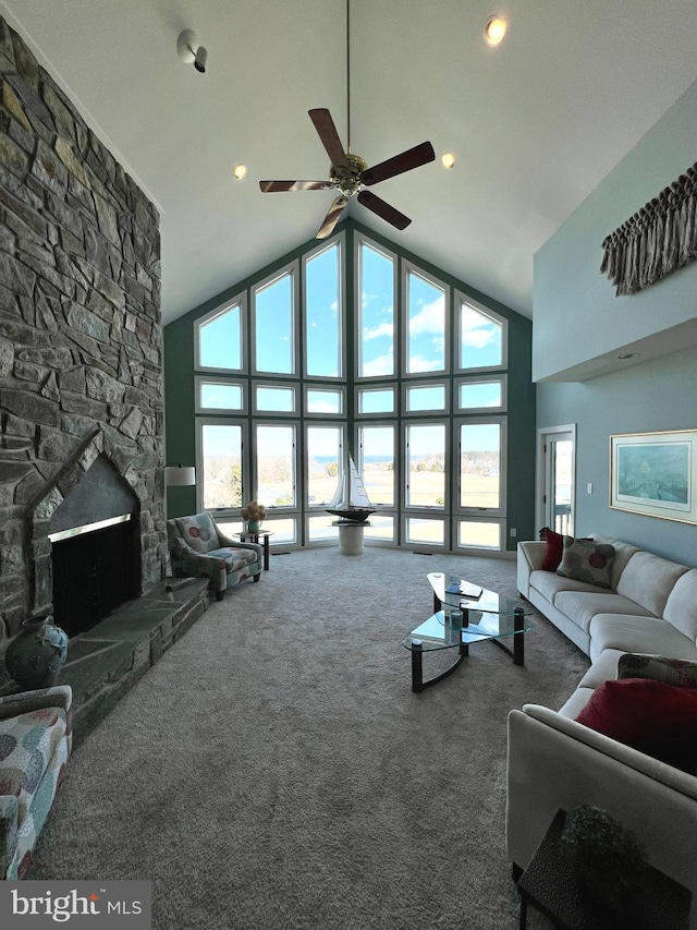 carpeted living area featuring a stone fireplace, high vaulted ceiling, and ceiling fan