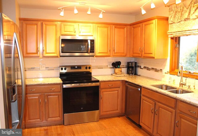 kitchen with light wood-style flooring, light stone countertops, stainless steel appliances, and a sink