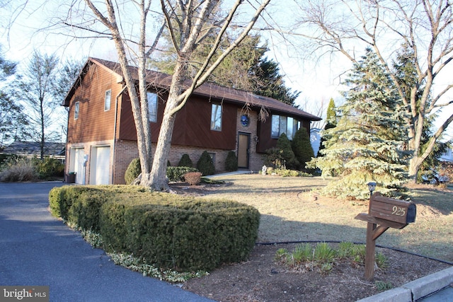 bi-level home featuring aphalt driveway, a garage, and brick siding