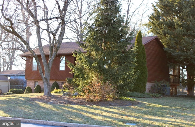 view of side of property featuring brick siding, a lawn, and fence