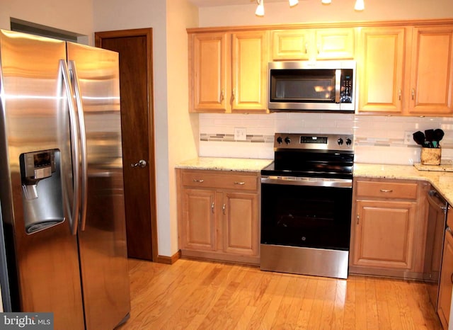 kitchen with light wood-style floors, stainless steel appliances, light stone countertops, and tasteful backsplash