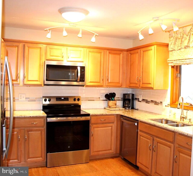 kitchen featuring light stone counters, a sink, stainless steel appliances, tasteful backsplash, and light wood-type flooring