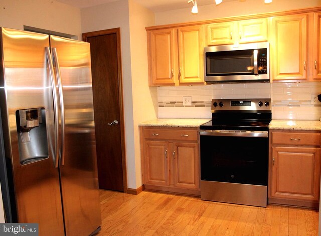 kitchen with light stone counters, decorative backsplash, appliances with stainless steel finishes, and light wood finished floors