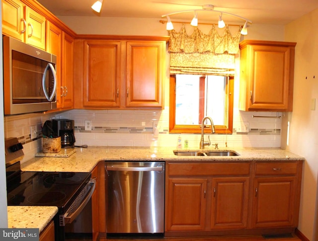 kitchen with light stone counters, backsplash, appliances with stainless steel finishes, and a sink