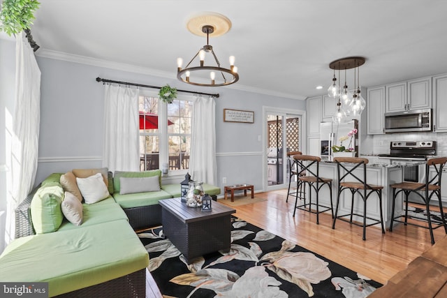 living area with light wood-style floors, an inviting chandelier, and ornamental molding