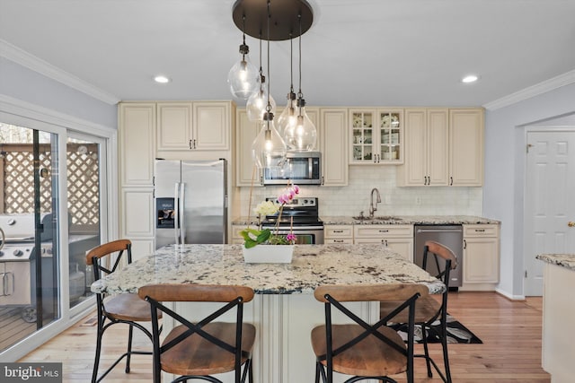 kitchen with a sink, cream cabinets, light wood-style floors, appliances with stainless steel finishes, and crown molding