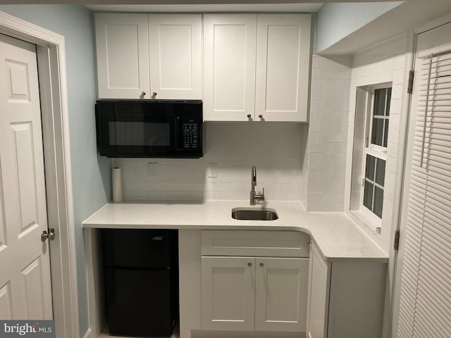 kitchen featuring black appliances, a sink, tasteful backsplash, white cabinets, and light countertops