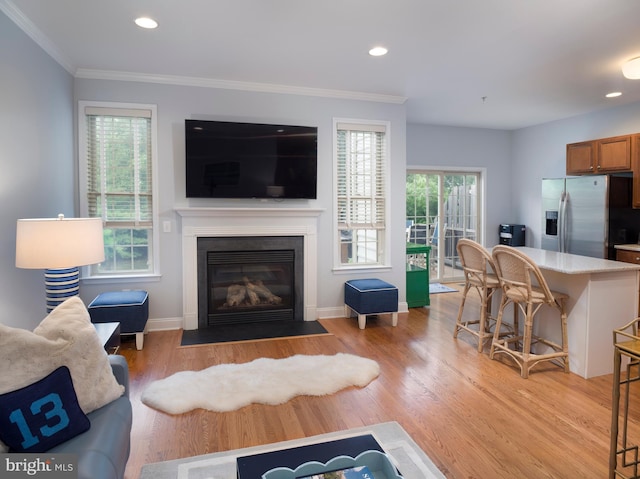 living area featuring a wealth of natural light, a fireplace with flush hearth, light wood-style floors, and ornamental molding