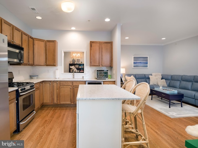 kitchen with a kitchen bar, visible vents, open floor plan, stainless steel appliances, and light wood-style floors