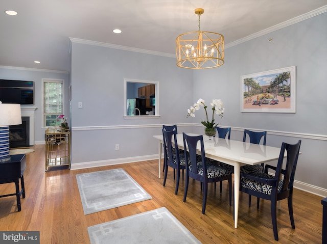 dining room with a glass covered fireplace, baseboards, wood finished floors, and crown molding