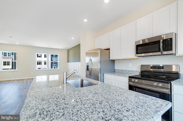 kitchen with recessed lighting, stainless steel appliances, wood finished floors, a sink, and white cabinets