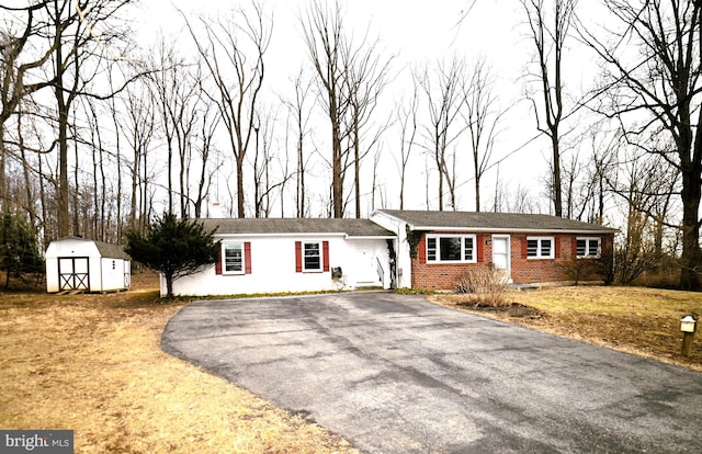 single story home featuring aphalt driveway, brick siding, an outdoor structure, and a shed