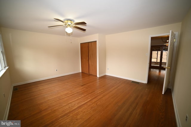 unfurnished bedroom with dark wood finished floors, visible vents, a closet, and baseboards