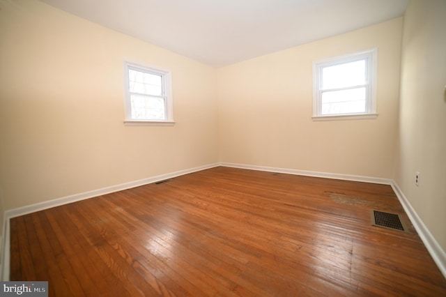 empty room featuring a wealth of natural light, visible vents, baseboards, and hardwood / wood-style floors