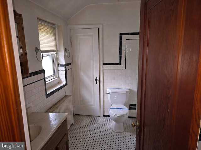 bathroom with tile walls, toilet, radiator heating unit, vaulted ceiling, and vanity