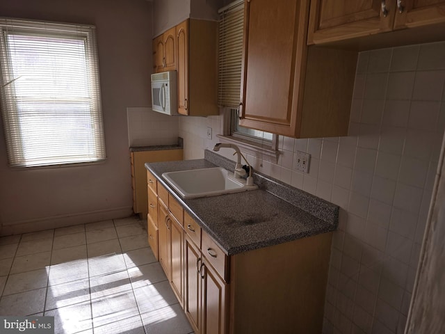 kitchen with light tile patterned floors, a sink, backsplash, and white microwave