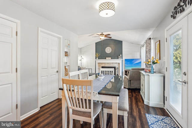 dining area featuring wood finished floors, baseboards, lofted ceiling, ceiling fan, and a stone fireplace