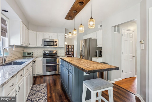 kitchen featuring a sink, backsplash, white cabinetry, appliances with stainless steel finishes, and butcher block counters