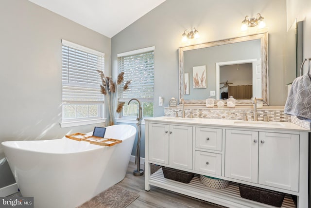 bathroom with backsplash, double vanity, vaulted ceiling, a soaking tub, and a sink