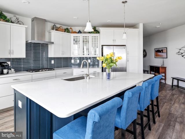 kitchen with a sink, freestanding refrigerator, wall chimney exhaust hood, black stovetop, and dark wood finished floors