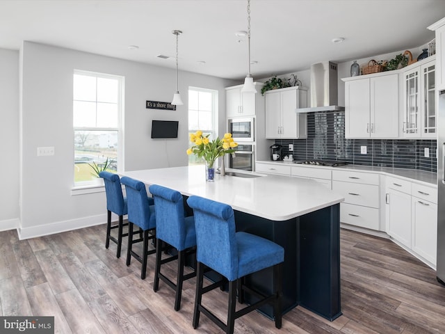 kitchen featuring a center island, dark wood-style flooring, backsplash, appliances with stainless steel finishes, and wall chimney range hood