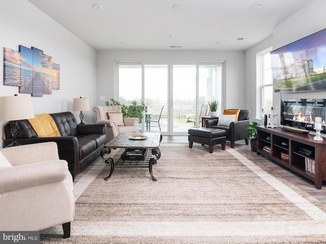 living area with a glass covered fireplace, wood finished floors, and visible vents