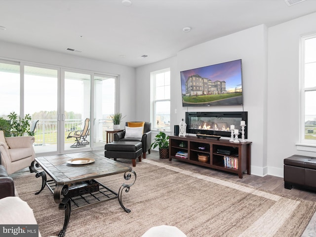 living area with a glass covered fireplace, visible vents, baseboards, and wood finished floors