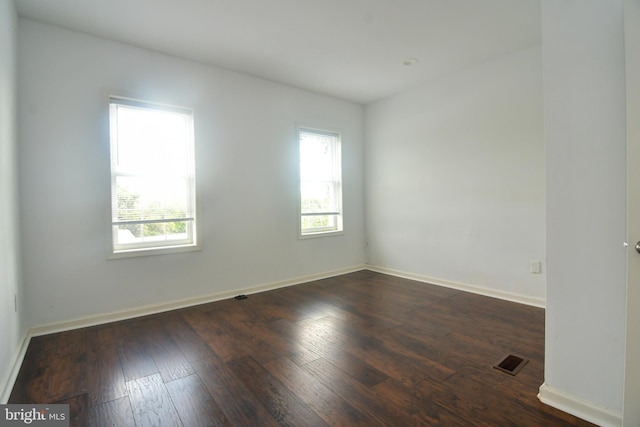 spare room featuring visible vents, baseboards, and dark wood-style flooring