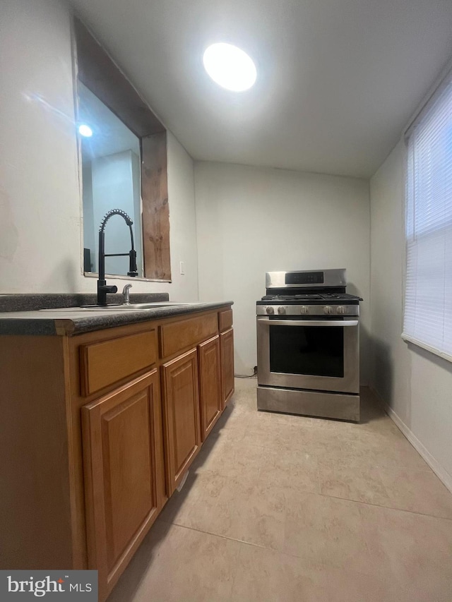 kitchen featuring dark countertops, brown cabinetry, stainless steel gas stove, a sink, and baseboards