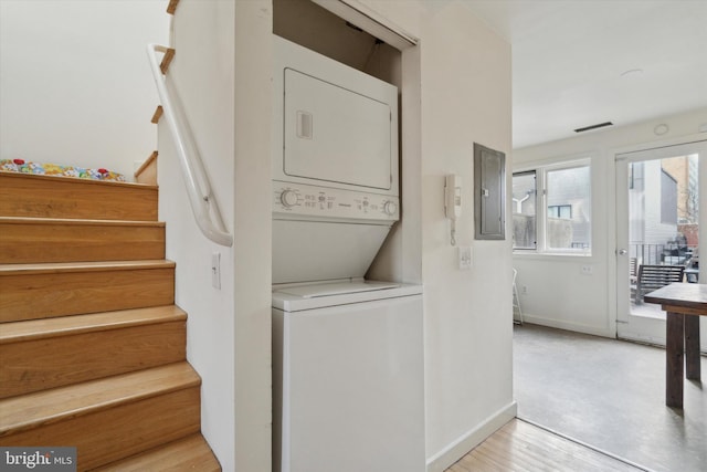 laundry room featuring stacked washer / drying machine, laundry area, electric panel, and baseboards