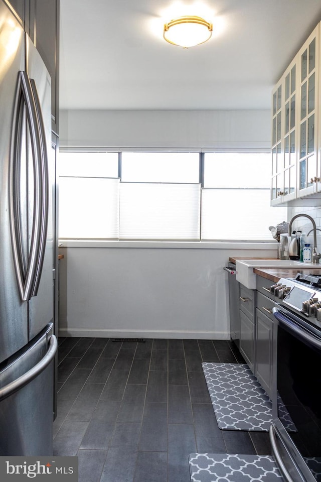 kitchen with glass insert cabinets, baseboards, appliances with stainless steel finishes, and a sink