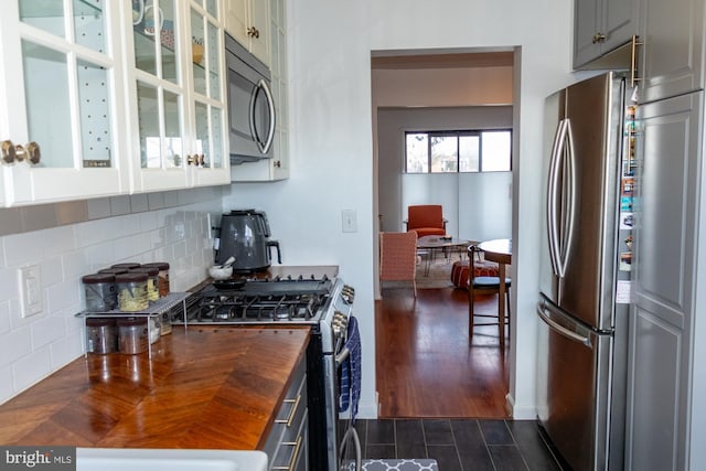 kitchen with dark wood finished floors, decorative backsplash, butcher block countertops, glass insert cabinets, and stainless steel appliances