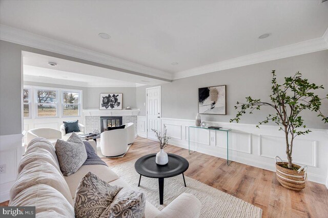 living area featuring light wood-style floors, a brick fireplace, ornamental molding, and wainscoting