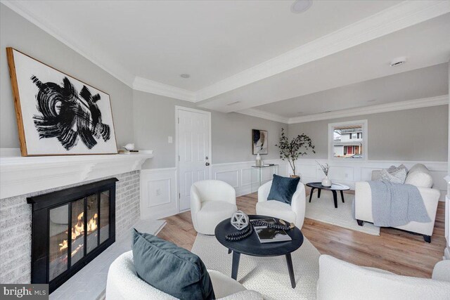 living area featuring a wainscoted wall, a brick fireplace, wood finished floors, and ornamental molding