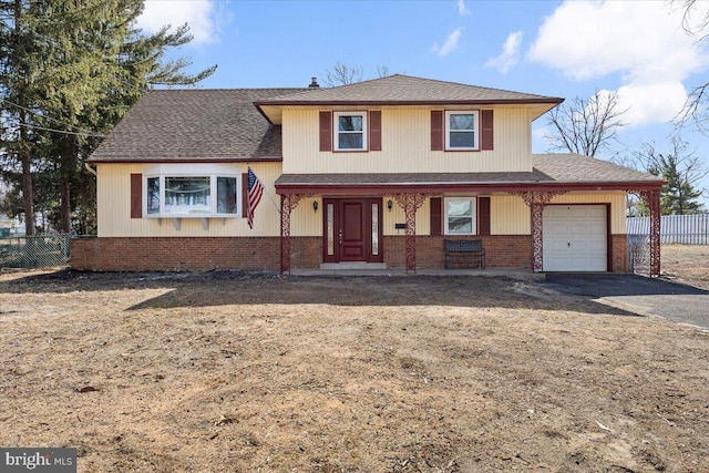 tri-level home featuring brick siding, covered porch, a garage, and fence