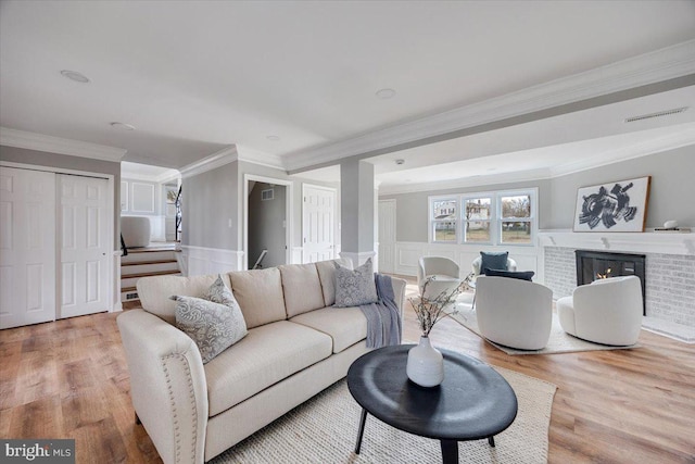 living room featuring visible vents, a wainscoted wall, wood finished floors, a brick fireplace, and stairs